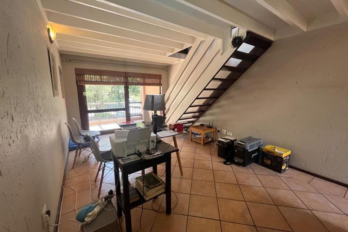 Open-plan living area featuring terracotta floor tiles, an exposed beam ceiling, and a staircase leading to the upper level with access to a balcony.