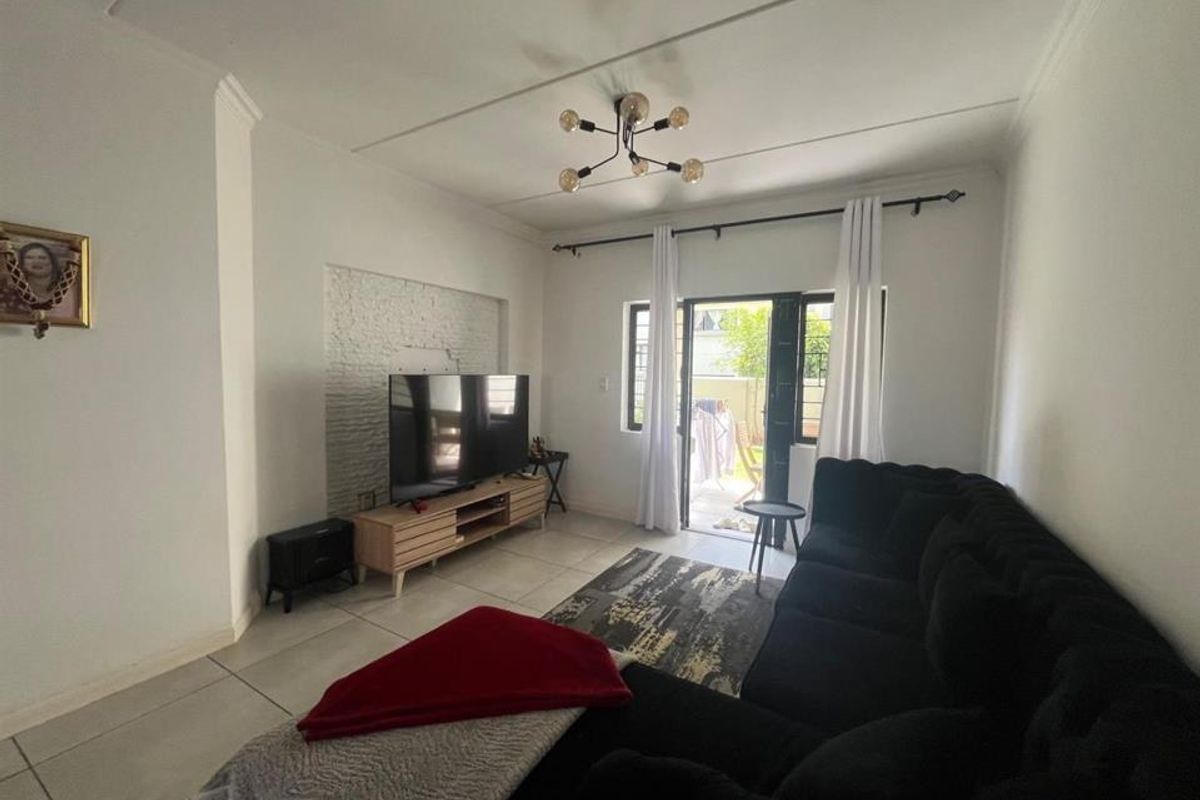 A bright living room featuring tiled flooring, an exposed brick feature wall, and a sliding glass door providing access to the outdoor area.