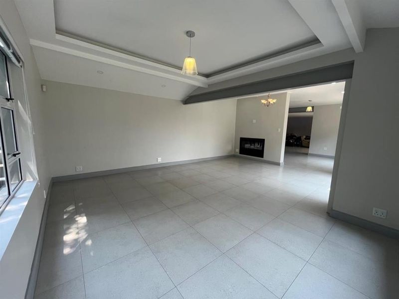 Spacious, open-plan living area featuring neutral tiled flooring, a modern tray ceiling with recessed lighting, and a built-in fireplace.