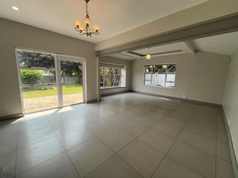 Spacious, light-filled living area featuring large format floor tiles, coffered ceilings, and direct access to the garden through sliding glass doors.