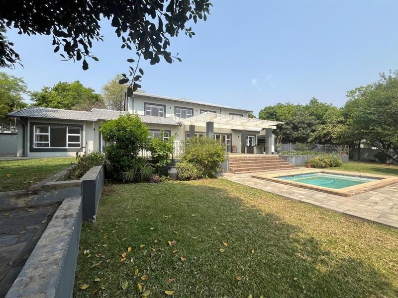 Rear view of the property featuring a landscaped garden, swimming pool, paved patio area, and a covered pergola structure.