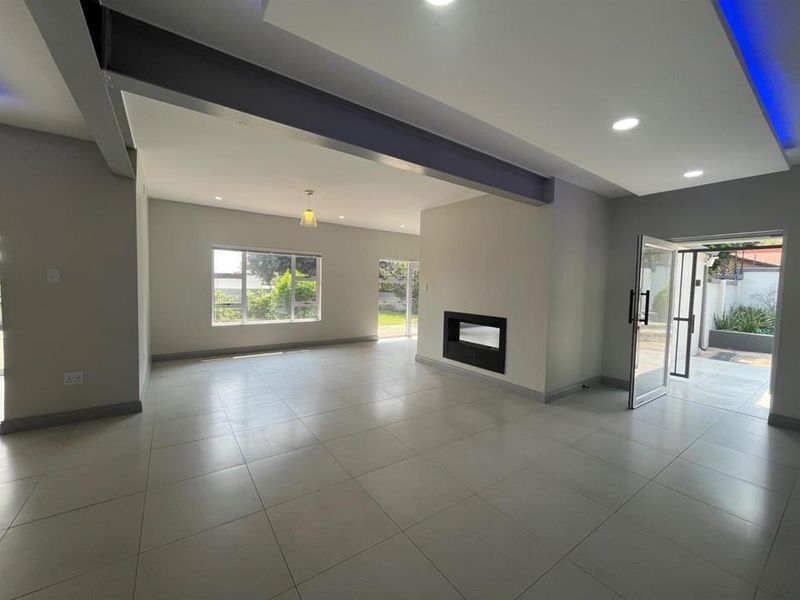 Spacious open-plan living area featuring modern tiled flooring, recessed ceiling lighting, a built-in fireplace, and an exposed structural steel beam.