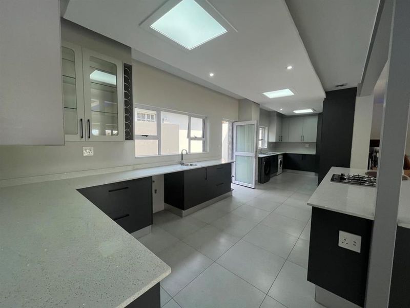 Modern, spacious kitchen featuring sleek dark cabinetry, light quartz countertops, integrated gas hob, tiled flooring, and ample natural light from skylights and windows.