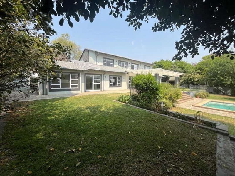 Rear view of the property featuring a spacious garden, swimming pool, paved patio area, and a pergola attached to the main house structure.