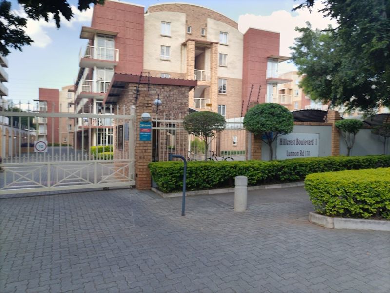 Front entrance view of Hillcrest Boulevard 1 apartment complex, featuring a secure gated access point, brick guardhouse, and paved driveway.