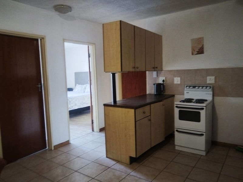 A compact kitchen featuring laminate cabinetry, tiled flooring, and a freestanding stove, with an adjacent view into the bedroom.
