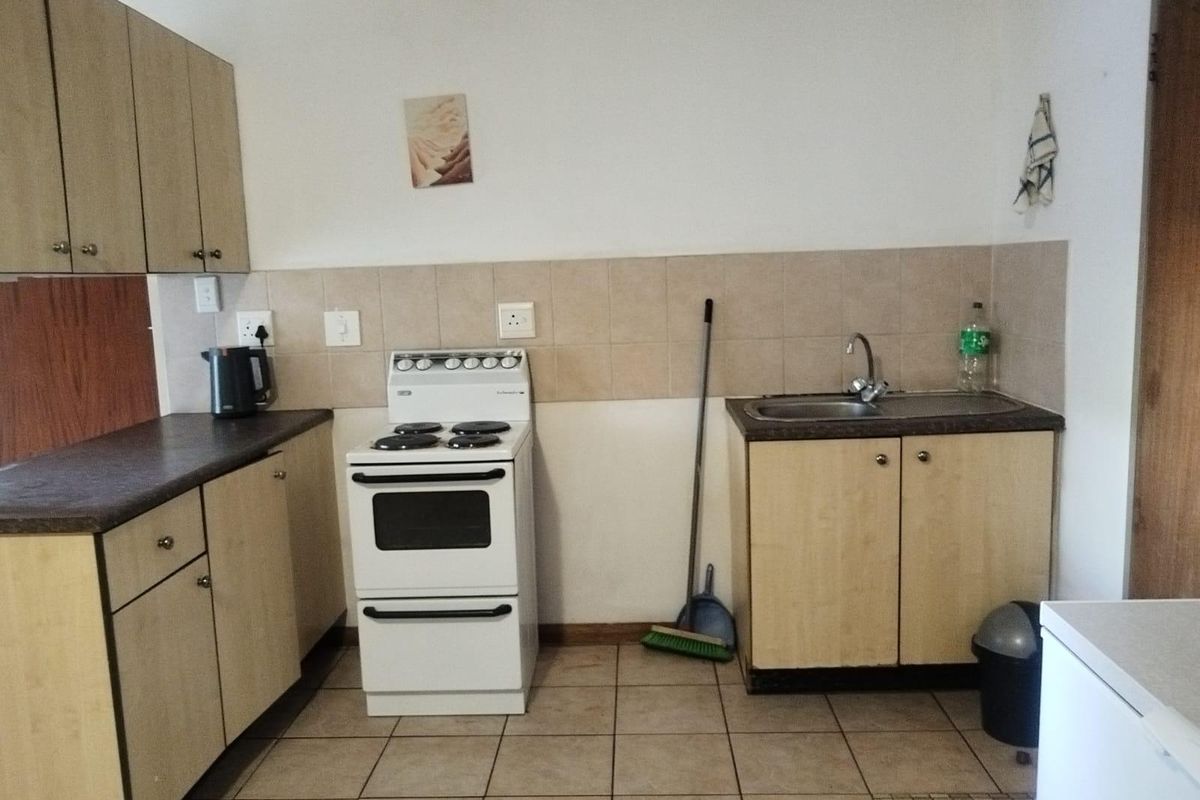 A functional kitchen featuring laminate cabinetry, a freestanding electric stove, stainless steel sink, and tiled backsplash with ceramic floor tiles.