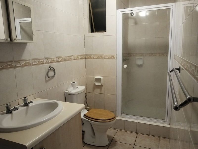A functional bathroom featuring a shower enclosure, vanity cabinet with basin, and tiled finishes throughout, offering a dated but practical layout.