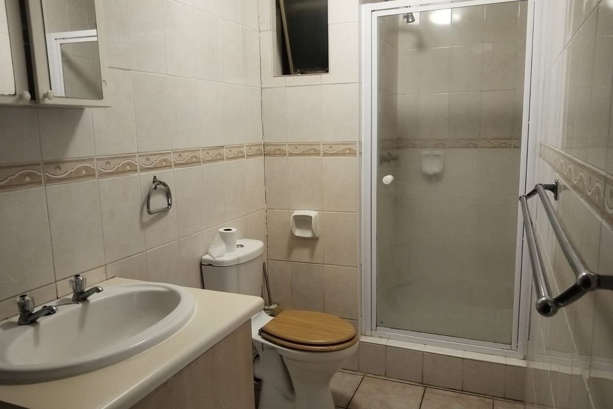 A functional bathroom featuring a shower enclosure, vanity cabinet with basin, and tiled finishes throughout, offering a dated but practical layout.