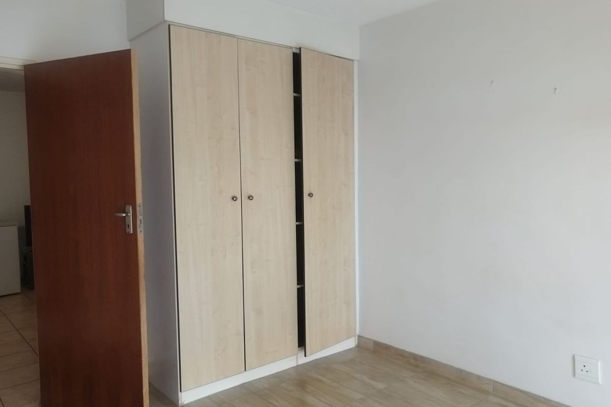 A clean, empty bedroom featuring light wood-finish built-in wardrobes, neutral walls, and tiled flooring.