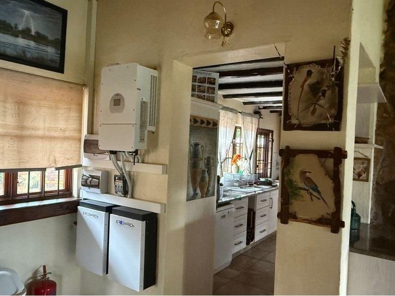 A kitchen area featuring exposed timber ceiling beams, tiled flooring, and integrated solar power infrastructure including an inverter and battery storage system.