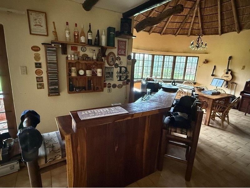 Rustic bar area featuring a built-in timber counter, traditional thatched roof with exposed beams, and tiled flooring, offering a cozy entertainment space.