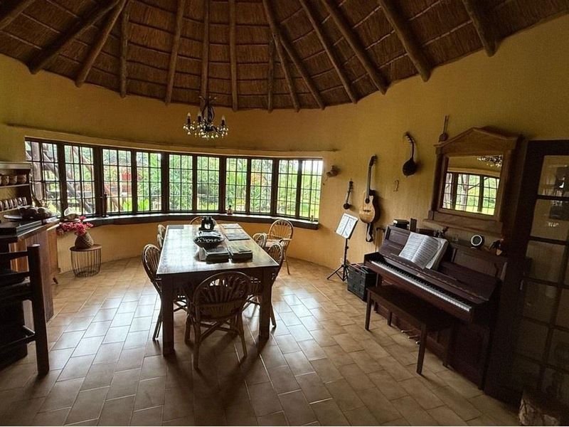 A spacious dining room featuring a unique thatched roof with exposed rafters, ceramic tile flooring, and large wrap-around windows providing natural light.
