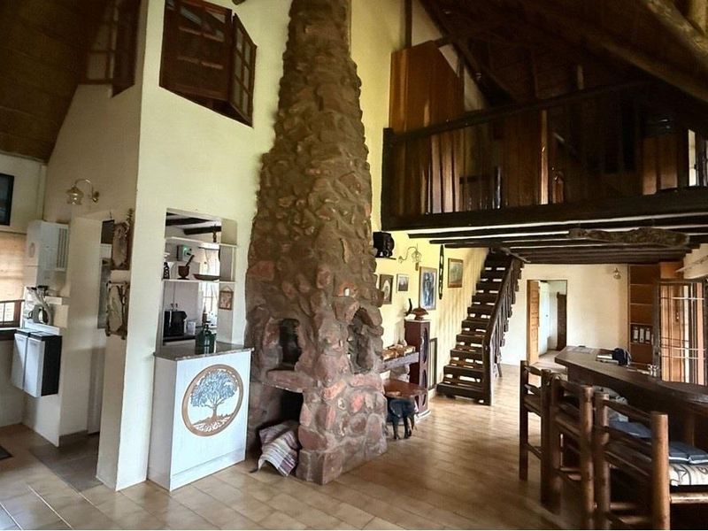 Spacious open-plan living area featuring a prominent stone fireplace, mezzanine level with timber balcony, and exposed ceiling beams, creating a rustic architectural aesthetic.