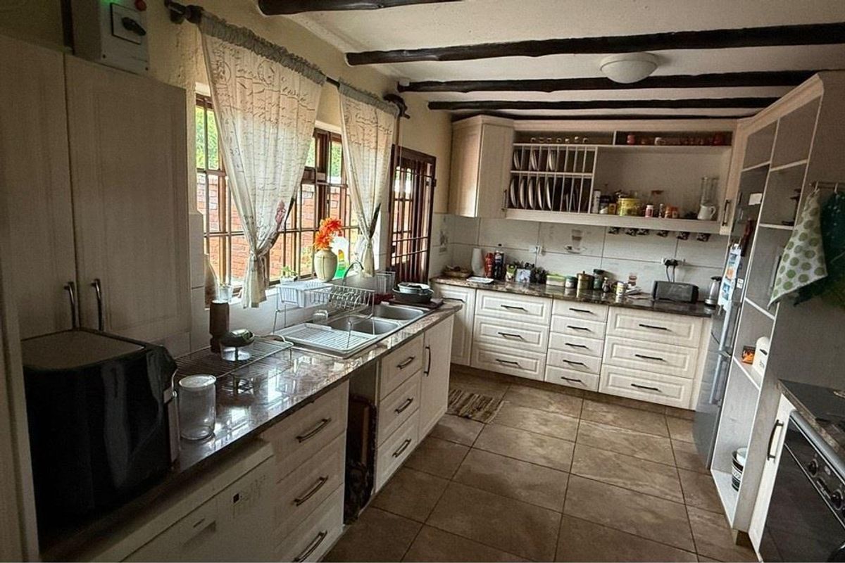 A rustic-style kitchen featuring exposed timber ceiling beams, granite countertops, ample built-in cabinetry, and tiled flooring with a functional layout.