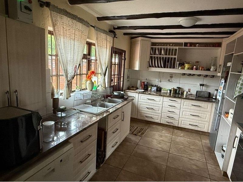 A rustic-style kitchen featuring exposed timber ceiling beams, granite countertops, ample built-in cabinetry, and tiled flooring with a functional layout.