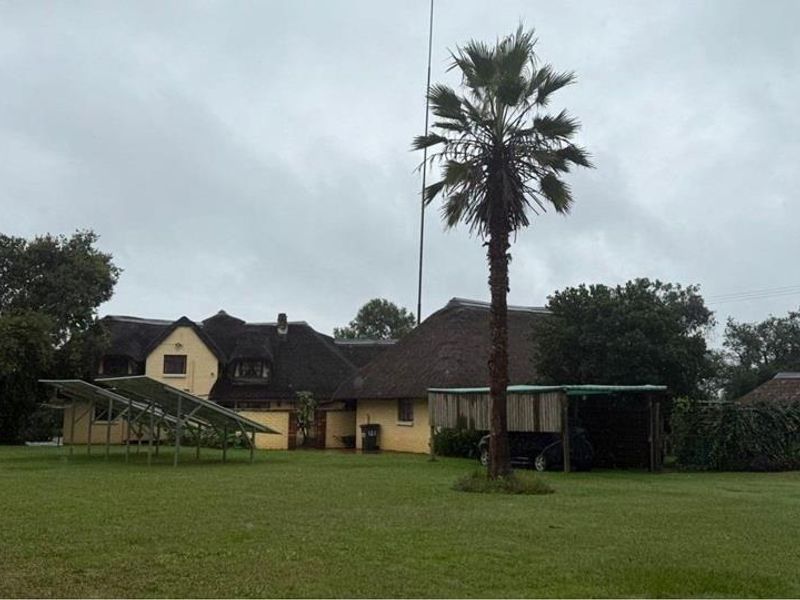 Rear view of the property featuring a traditional thatch roof, a large garden area, and a ground-mounted solar panel array.