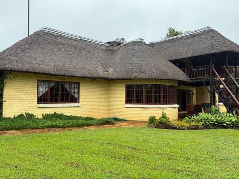Rear view of a traditional thatched-roof house featuring a timber balcony, external staircase, and established garden surroundings.