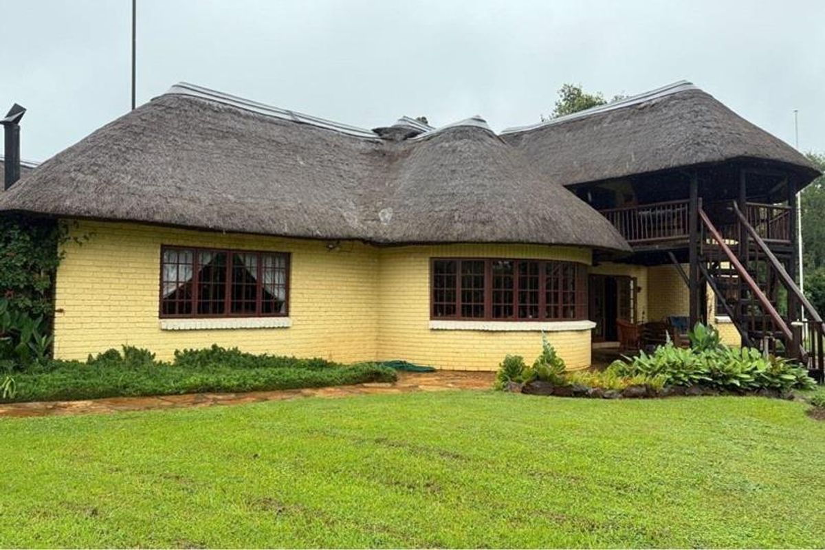 Rear view of a traditional thatched-roof house featuring a timber balcony, external staircase, and established garden surroundings.