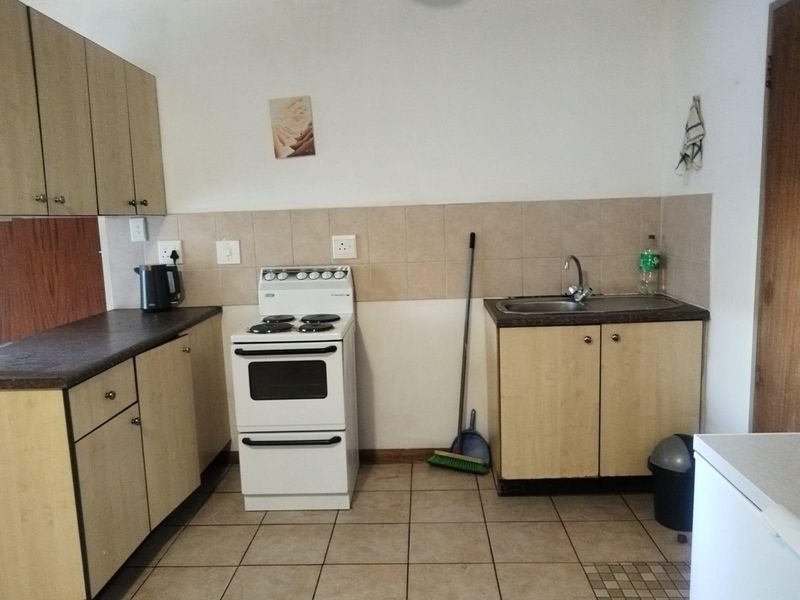 A functional kitchen featuring laminate cabinetry, a freestanding electric stove, stainless steel sink, and tiled backsplash with ceramic floor tiles.