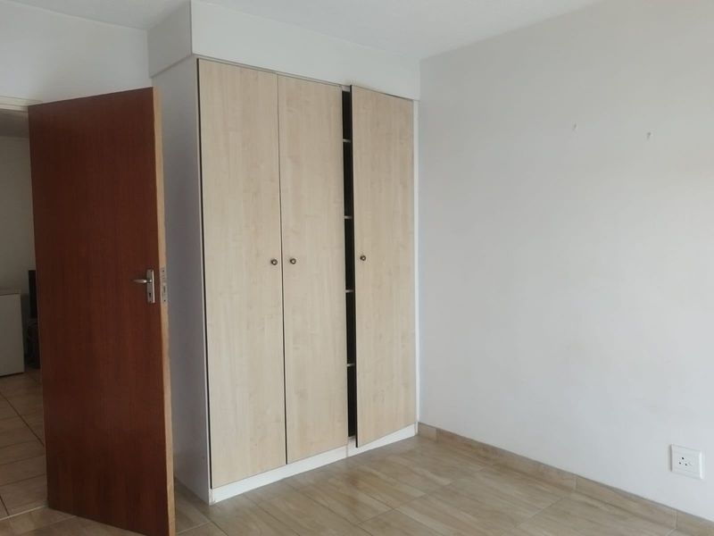 A clean, empty bedroom featuring light wood-finish built-in wardrobes, neutral walls, and tiled flooring.