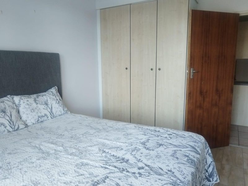 A bedroom featuring built-in cupboards, tiled flooring, and a wooden door, offering a functional and neutral living space.