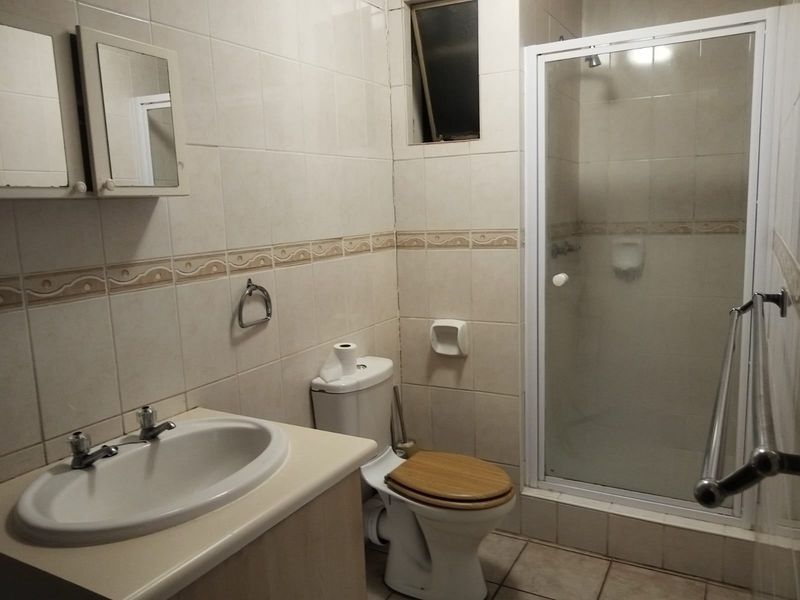 A functional bathroom featuring a vanity basin, toilet, and a glass-enclosed shower with neutral wall tiling and tiled flooring.