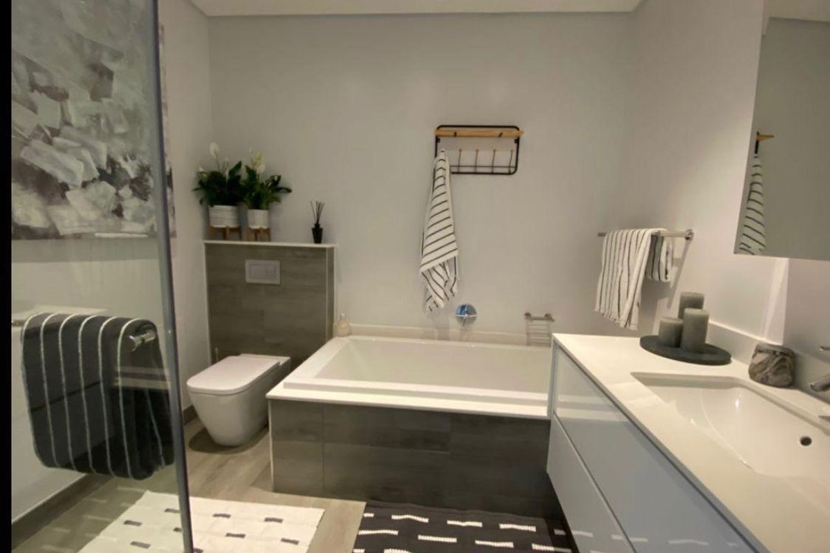 Modern bathroom featuring a built-in bathtub, wall-hung toilet, and a sleek vanity with an integrated basin and glass shower enclosure.