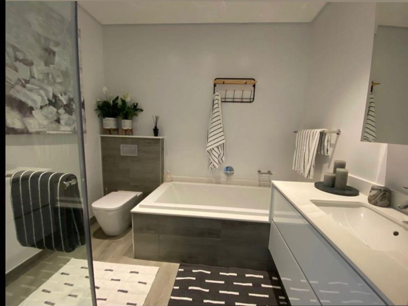 Modern bathroom featuring a built-in bathtub, wall-hung toilet, and a sleek vanity with an integrated basin and glass shower enclosure.