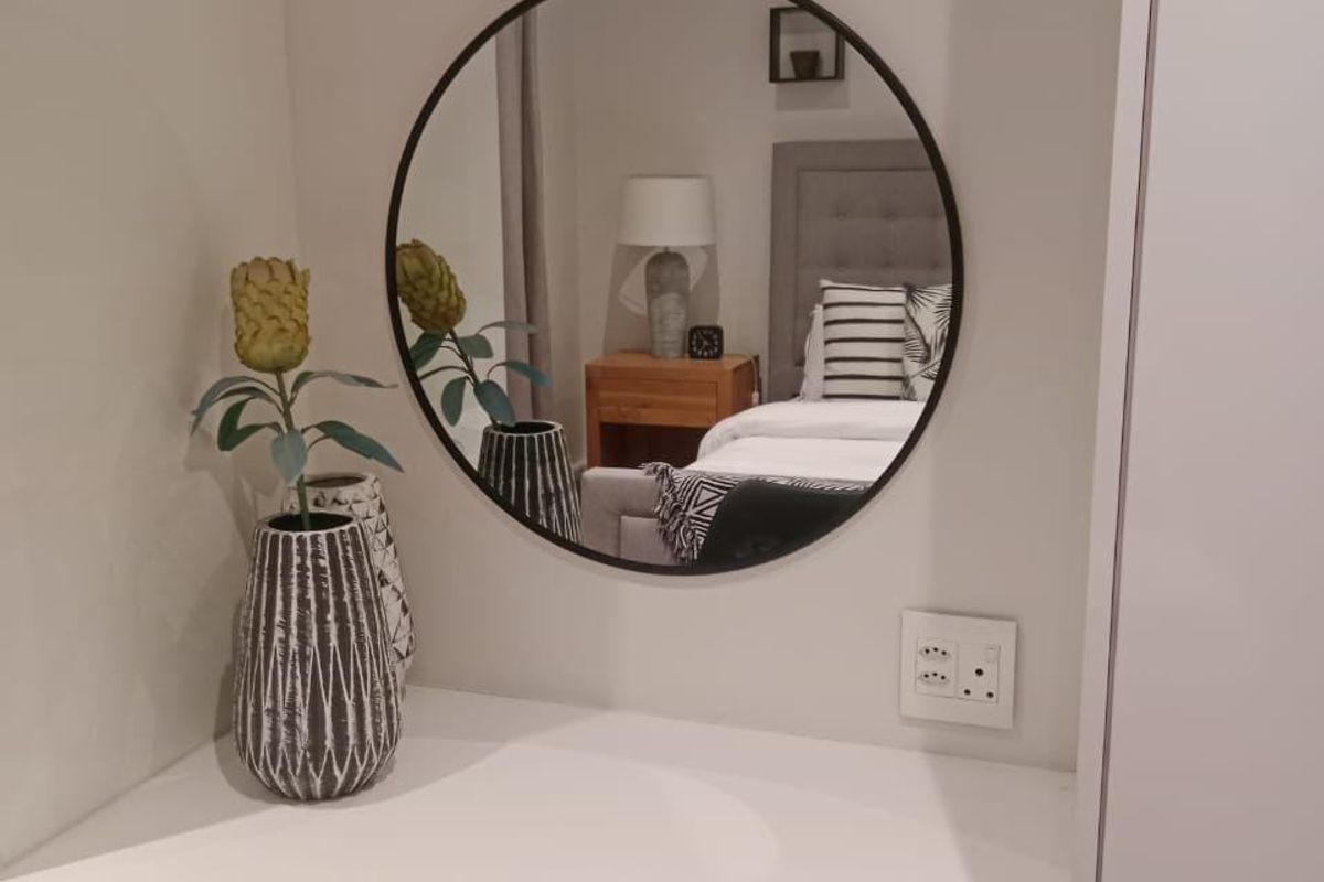 A well-maintained bedroom vanity area featuring a built-in desk, wall-mounted mirror, and integrated electrical outlets.