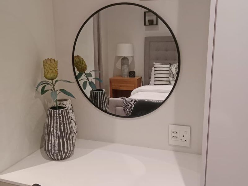 A well-maintained bedroom vanity area featuring a built-in desk, wall-mounted mirror, and integrated electrical outlets.