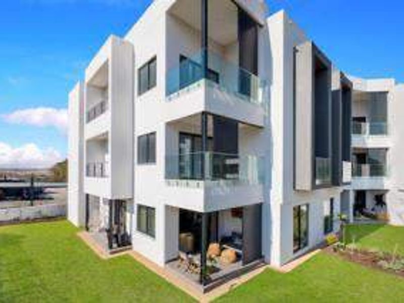 A modern multi-story apartment building featuring clean white architectural lines, glass-fronted balconies, and well-maintained surrounding lawn areas.