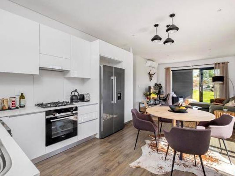 Modern open-plan kitchen and living area featuring sleek white cabinetry, integrated appliances, and seamless access to the outdoor patio through sliding glass doors.
