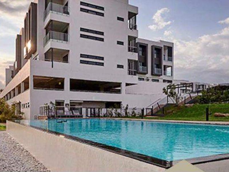 A modern apartment complex featuring a large swimming pool, glass balcony balustrades, and well-maintained landscaped grounds.