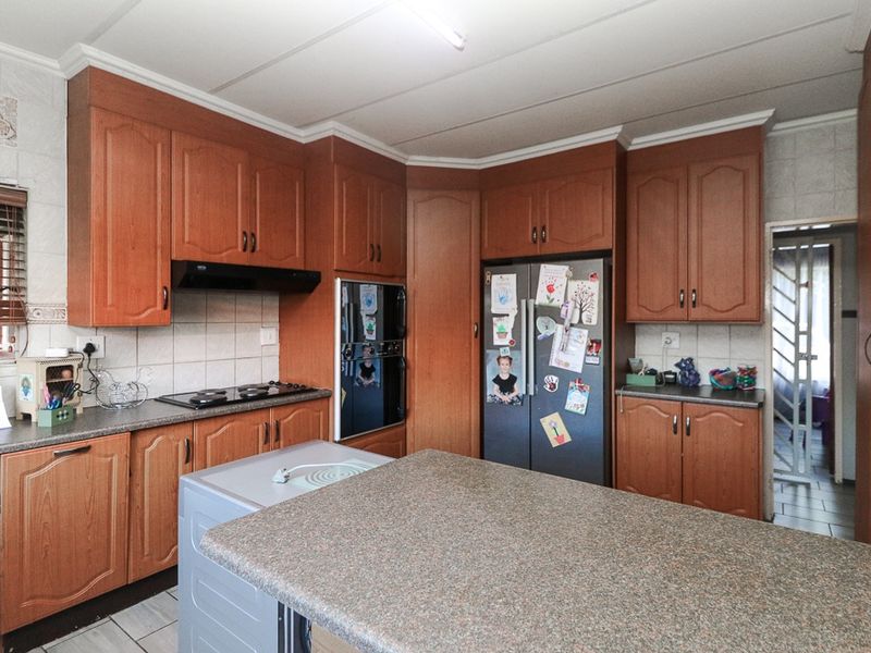 A functional kitchen featuring wood-finish cabinetry, built-in oven, hob, extractor fan, and a central island with laminate countertops.