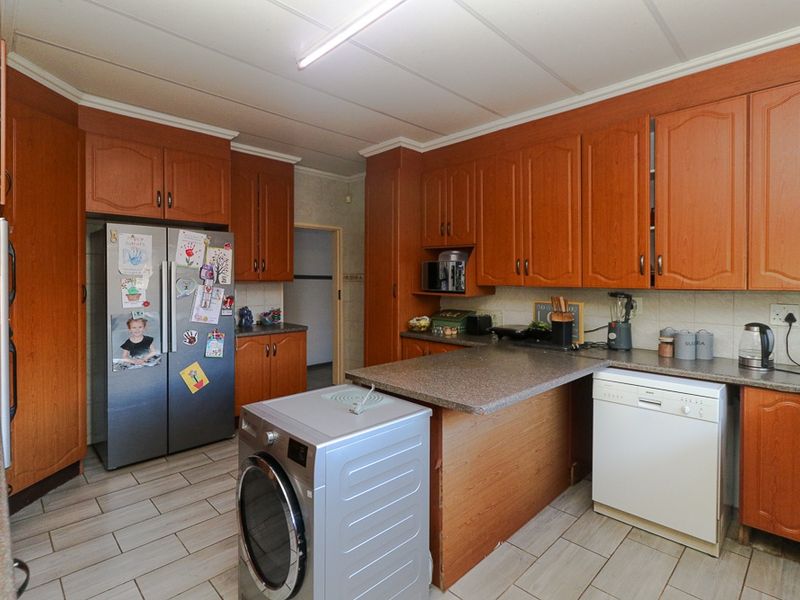 A functional kitchen featuring wood-toned cabinetry, laminate countertops, tiled flooring, and integrated space for laundry appliances.