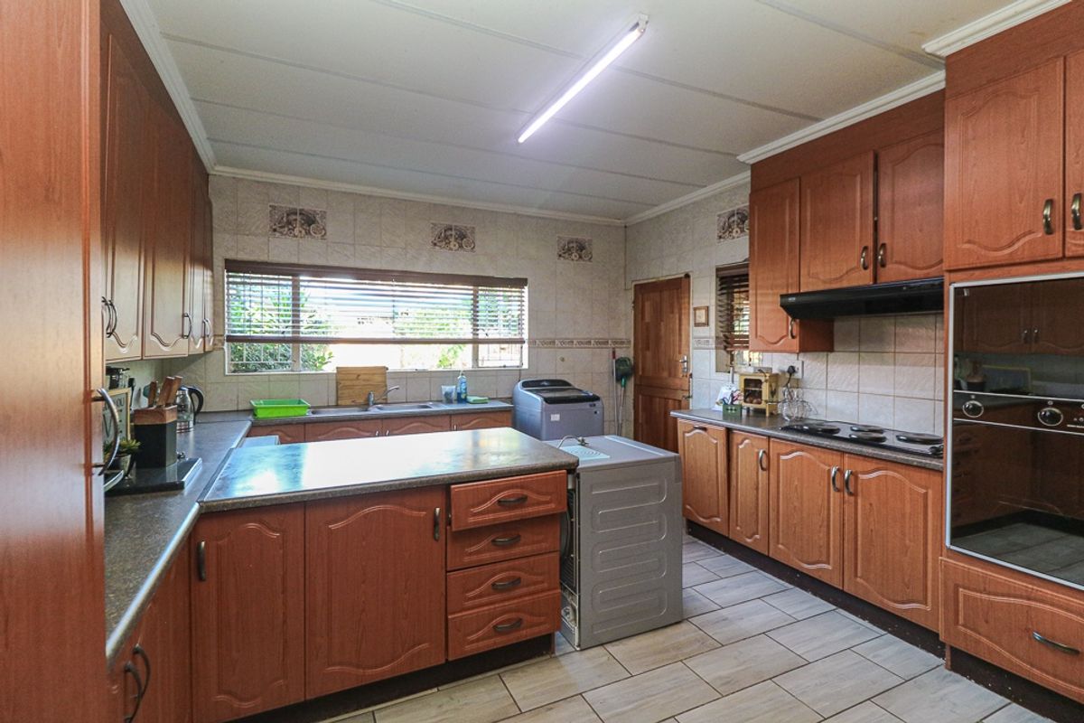 A functional kitchen featuring wood-finish cabinetry, built-in oven, hob, extractor fan, and tiled flooring with ample counter space.