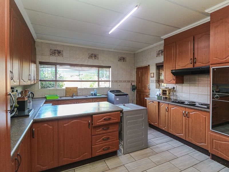 A functional kitchen featuring wood-finish cabinetry, built-in oven, hob, extractor fan, and tiled flooring with ample counter space.