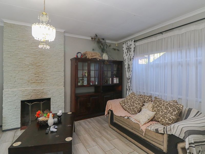A living room featuring a stone-clad fireplace, tiled flooring, and large windows with curtains.