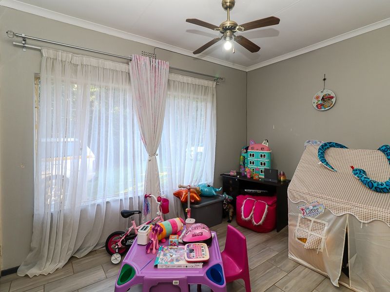 A functional bedroom featuring tiled flooring, a ceiling fan, and large windows with curtain rails, offering a versatile space for various uses.
