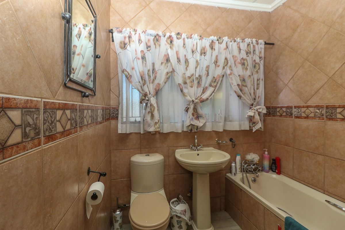 A compact bathroom featuring full-height wall tiling, a pedestal basin, a toilet, and a built-in bathtub with a shower mixer.
