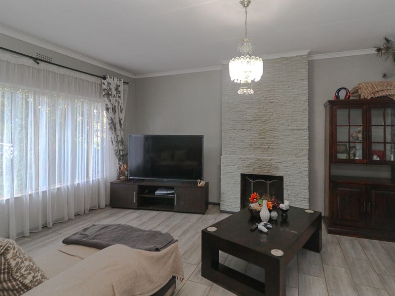 A comfortable living room featuring a stone-clad fireplace, tiled flooring, and a large window allowing for natural light.
