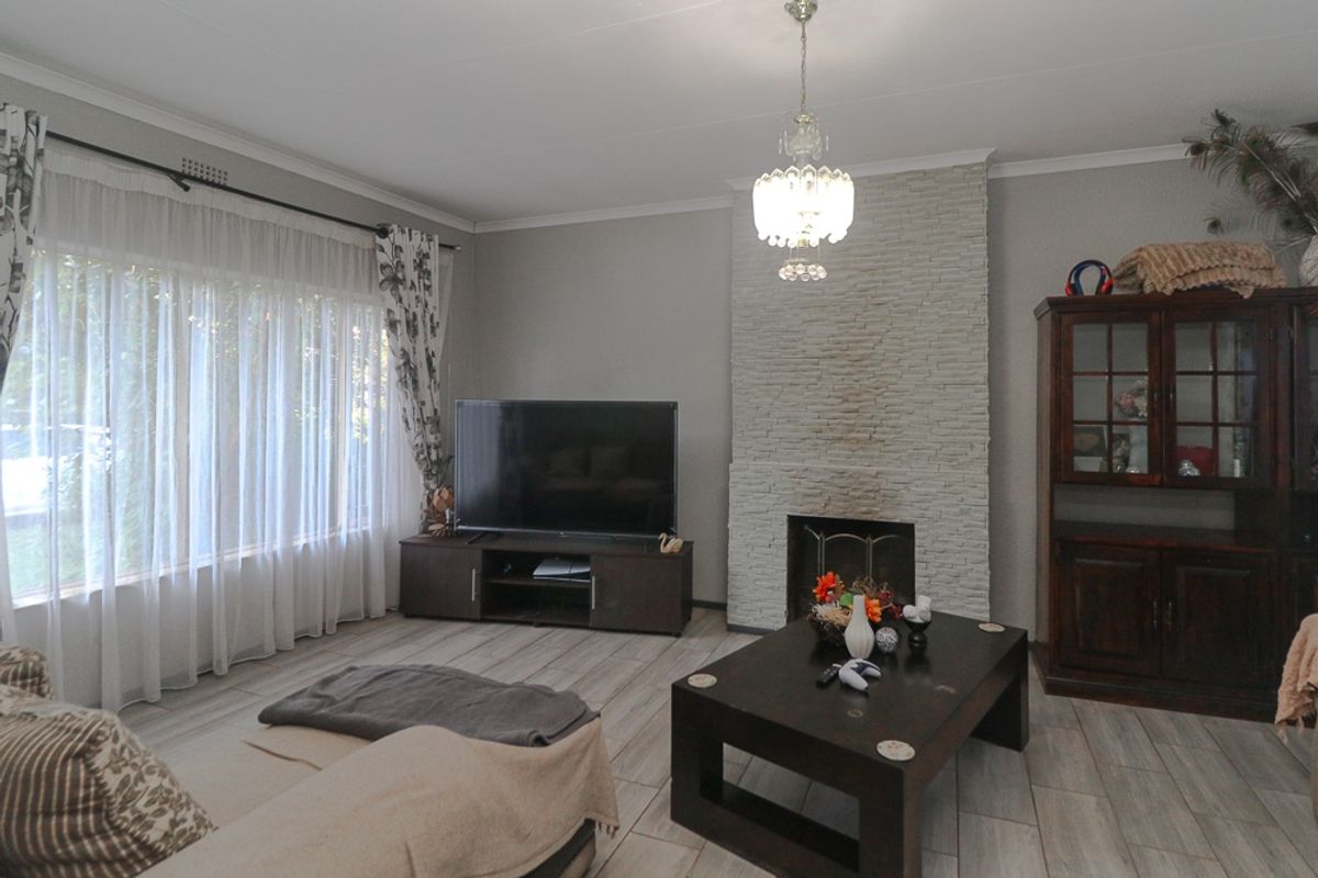A comfortable living room featuring a stone-clad fireplace, tiled flooring, and a large window allowing for natural light.