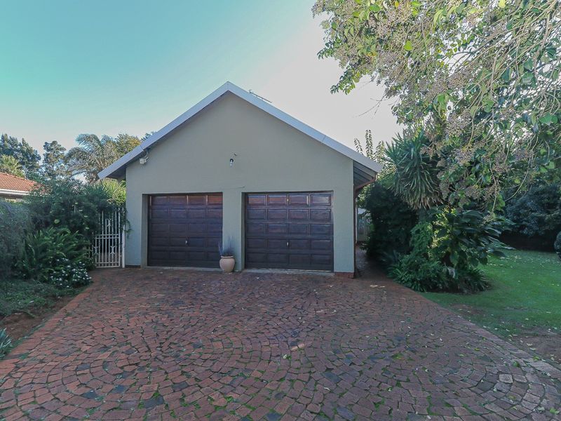 A detached double garage featuring two dark wood-finish sectional doors, set against a paved driveway and landscaped garden area.