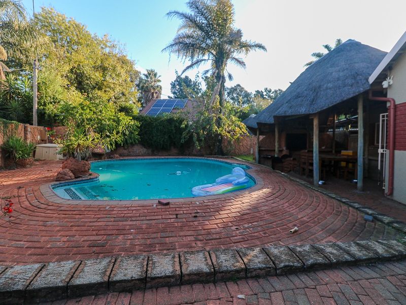 Outdoor pool area featuring a swimming pool, brick paved surround, and a covered thatch patio area for entertaining.
