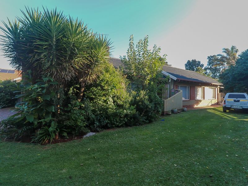 A view of the property's exterior front facade, featuring a tiled roof, brick wall construction, and a well-maintained lawn with established garden landscaping.