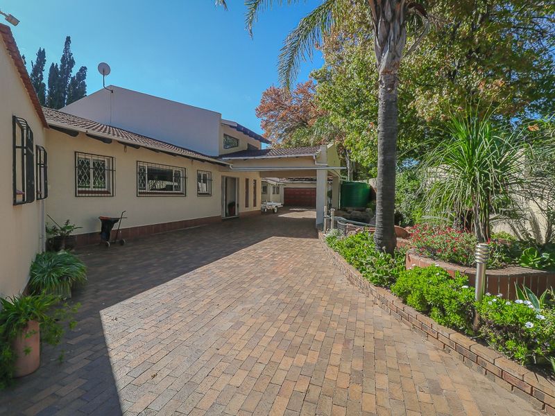 A paved driveway leading to a carport and the front entrance of the house, featuring established garden beds and security features.