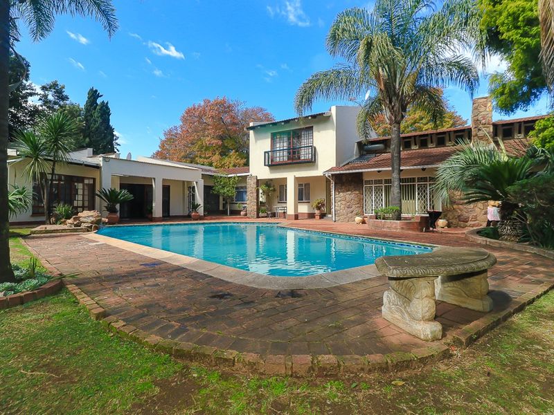Spacious outdoor pool area featuring brick paving, stone-clad exterior walls, and a balcony overlooking the swimming pool and landscaped garden.