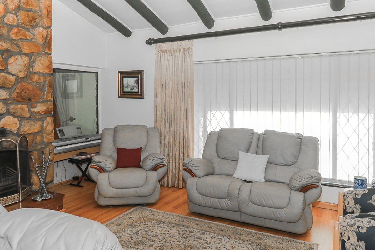 A cozy living room featuring a prominent stone fireplace, exposed ceiling beams, and laminate flooring, offering a warm and traditional atmosphere.