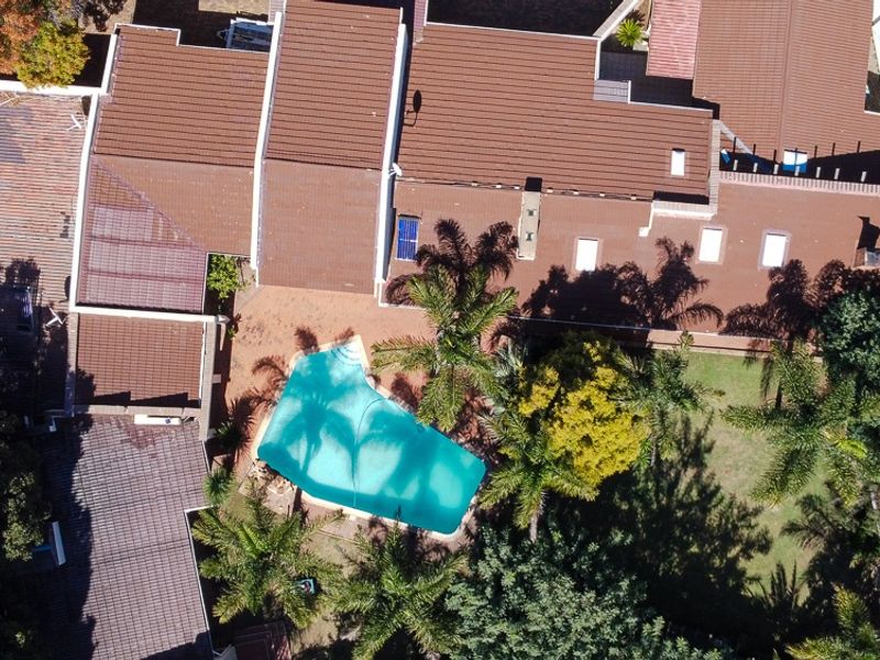 Aerial view of the property showcasing the tiled roof structure, swimming pool, and surrounding garden area.